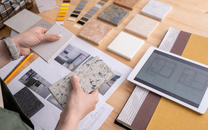 Photo of hands of interior designer holding and comparing materials with more options on table in front of them